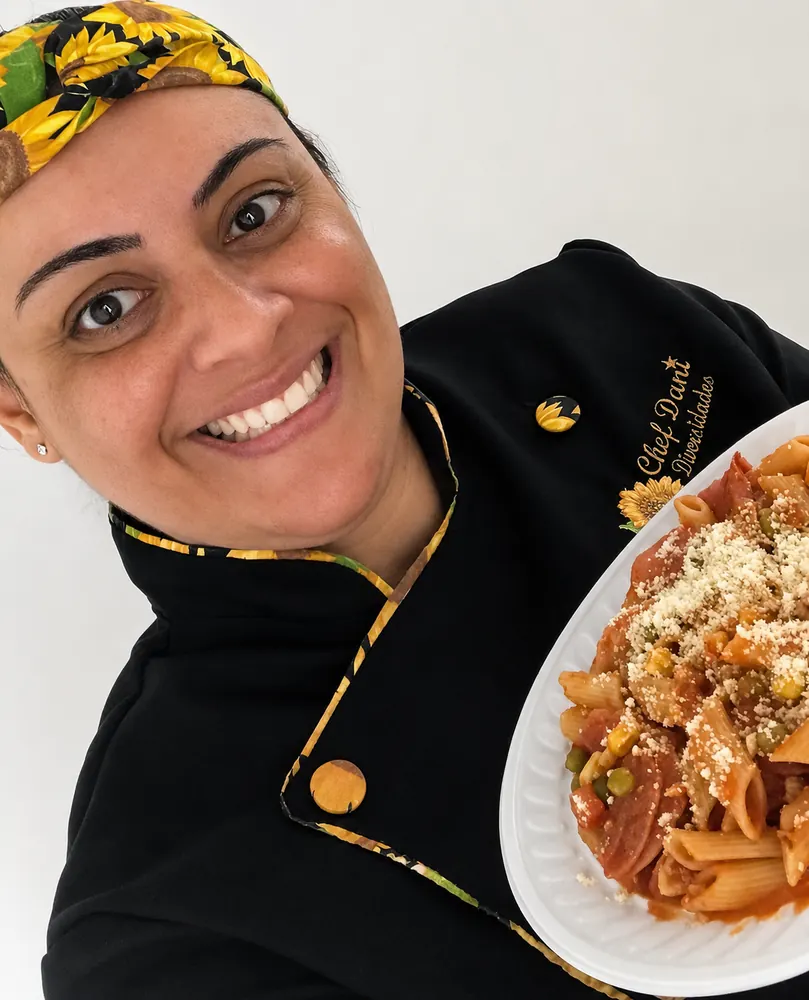 Daniela Moura, dona do Buffet Dani Diversidades, de dólmã de chef segurando um prato